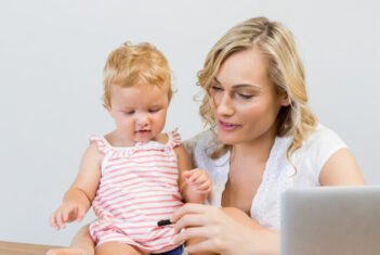 Mother holding baby girl while writing notes on paper